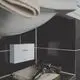 Weiße Vaillant-Anlage montiert an einer Wand, daneben ein Föhn auf einem Handtuch. Der Bereich ist mit dunklen Fliesen und einem Waschbecken ausgestattet.
